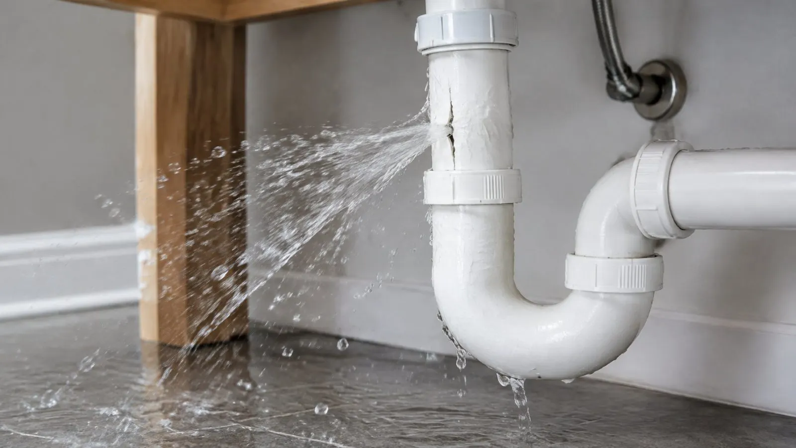 Water spraying from a leaking drain pipe onto a tile floor